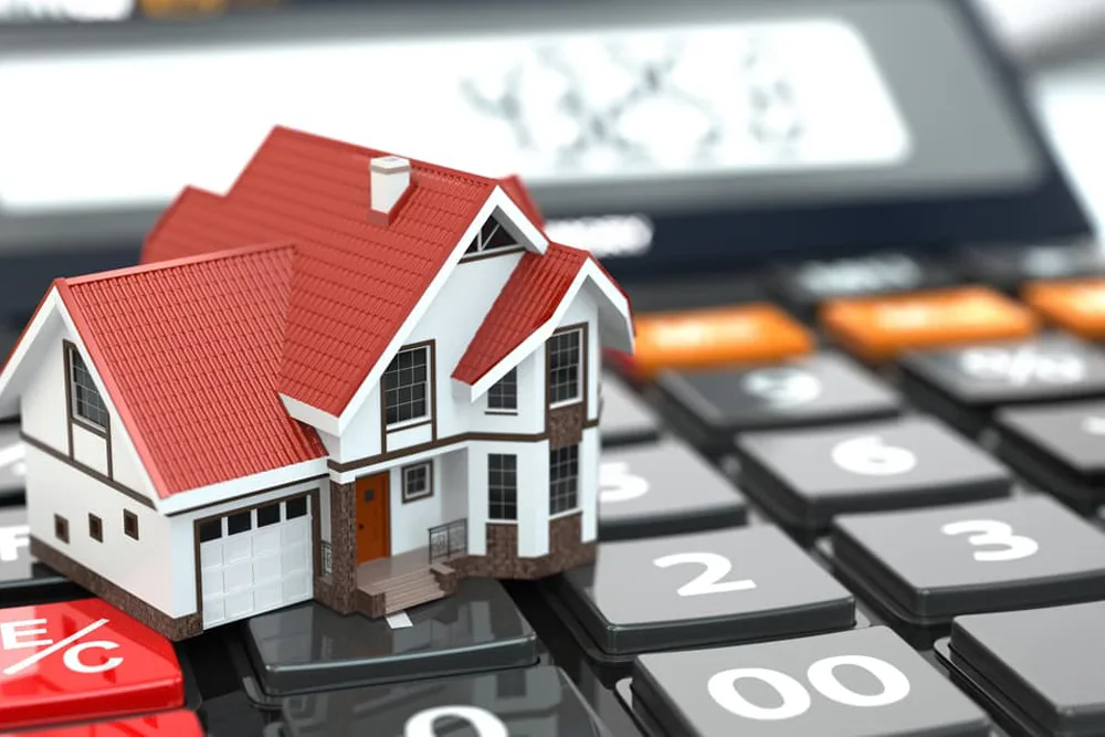 Miniature house with red roof on calculator, representing home finance.