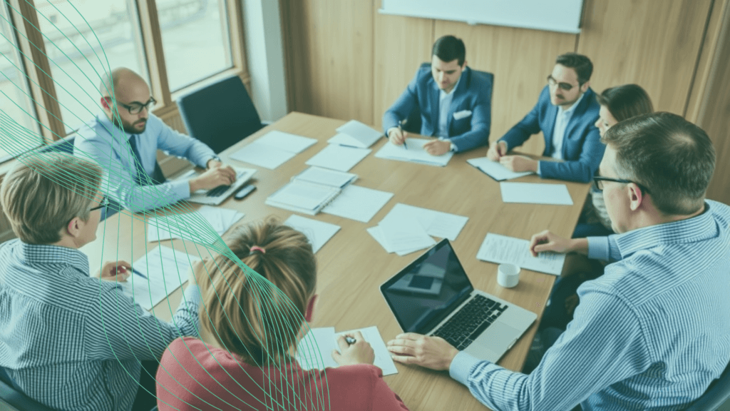 A board meeting around a table with papers and a laptop.