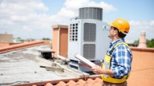 A technician checks a building rooftop air unit with a clipboard in hand