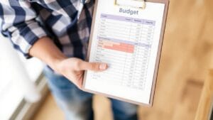 A person holds a clipboard and points at a printed budget sheet